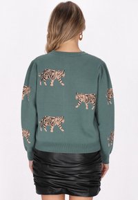 Jersey de punto verde con motivos de tigre a rayas rosa y negra. Presenta mangas largas y un escote redondo. Combinado con una falda plisada negra.