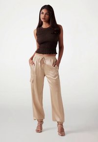 Top marrón con fruncido combinado con pantalones cargo sueltos de color beige claro, con bolsillos y cintura con cordón. Modelo con sandalias de tiras.