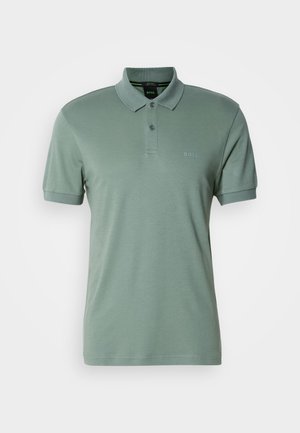 Šviesiai žalia polo marškinėlių, pagamintų iš minkštos medžiagos, trumpomis rankovėmis, su įrengtu apykakle, dviejų mygtukų užtrauktuku ir subtiliu logotipo ženkleliu ant krūtinės.