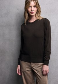 Dunkelbrauner Pullover mit langen Ärmeln, Rippkragen und -bündchen. Glatte Textur, taillierte Passform, kombiniert mit hellbraunen, maßgeschneiderten Hosen.