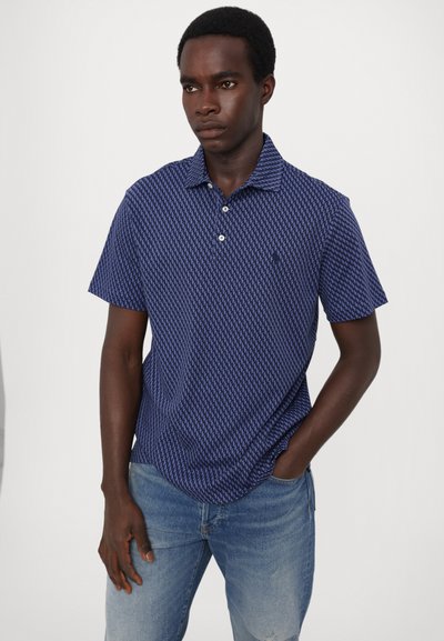 Ναυτικό polo μπλουζάκι με γεωμετρικό σχέδιο, κοντά μανίκια και καμπυλωτό γιακά. Διαθέτει δύο κουμπιά και άνετη εφαρμογή. Φορεμένο με ανοιχτό μπλε τζιν.