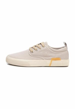 Zapatillas de lona beige con punta redonda, cinco ojales y acento color amarillo en el talón. Suela de goma texturizada con patrón estriado.