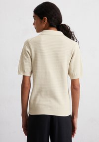 Beige gebreide poloshirt met korte mouwen en ribbelzoom, met een structuurpatroon en een klassieke kraag. Gemaakt naar een combinatie met donkere broeken.