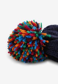Marine gebreide beanie met een fluffy, meerkleurige pompon bestaande uit rode, oranje, blauwe, groene en zwarte strengen. Zachte textuur en ronde vorm.