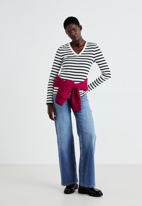 Haut rayé noir et blanc à manches longues avec un col en V, assorti à un jean en denim bleu à jambe large. Un sweat-shirt bordeaux noué à la taille.