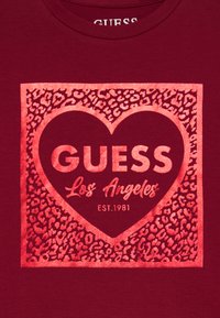 Bordo majica s metalik grafikom srca i printom leopard u kojoj se u raznim kontrastnim bojama ističe tekst "GUESS Los Angeles EST. 1981".