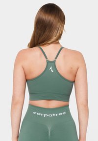 Zelen modrček za šport z zasnovo racerback, teksturirano blago in poudarkom na logotipu. Ima nastavljive naramnice in prilega se postavi.