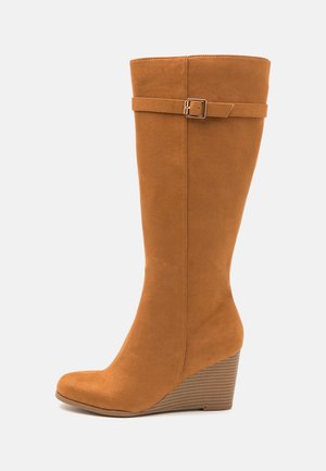 Keilabsatzstiefeletten aus weichem, hellbraunem Kunstwildleder, mit runder Zehenform, hohem Schaft, seitlichem Schnallenakzent und strukturiertem Keilabsatz.