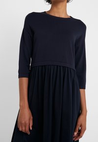 Abito navy con un corpetto aderente, scollatura rotonda, maniche a tre quarti e una gonna ampia e arricciata che arriva sotto il ginocchio.