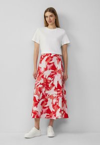 Jupe à motif floral rouge et blanc avec une conception enveloppante, portée avec un t-shirt blanc uni et des baskets blanches. Texture de tissu lisse.