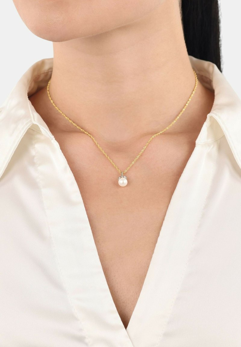 Guldhalsband med en tvistad design, som har en ensam vit pärla hängande i en silverkapsel. Bärs över en vit skjorta med krage.