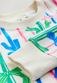 Bluza z kremowym tłem, ozdobiona żywymi, niebieskimi, różowymi i zielonymi abstrakcyjnymi wzorami. Żebrowany dekolt i mankiety o miękkiej fakturze.