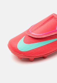 Červené syntetické kopačky na futbal s textúrovaným horným dielom a tyrkysovým logom Nike. Obsahujú suchý zips a tvarované gumové kolíky.