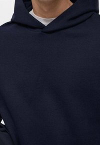 Granatowa bluza z kapturem wykonana z miękkiego materiału, posiadająca dużą kieszeń z przodu, kaptur ze sznurkiem oraz ściągacze przy rękawach, o luźnym kroju.