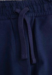 Granatowe dresy mają elastyczny pas ze sznurkiem, gładką teksturę oraz boczną kieszeń dla większej funkcjonalności.