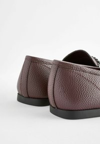Burgundy nahka kengät, joissa on teksturoitu pinta, pyöreät korot ja mustat kumipohjat. Ompeleet korostavat reunoja.