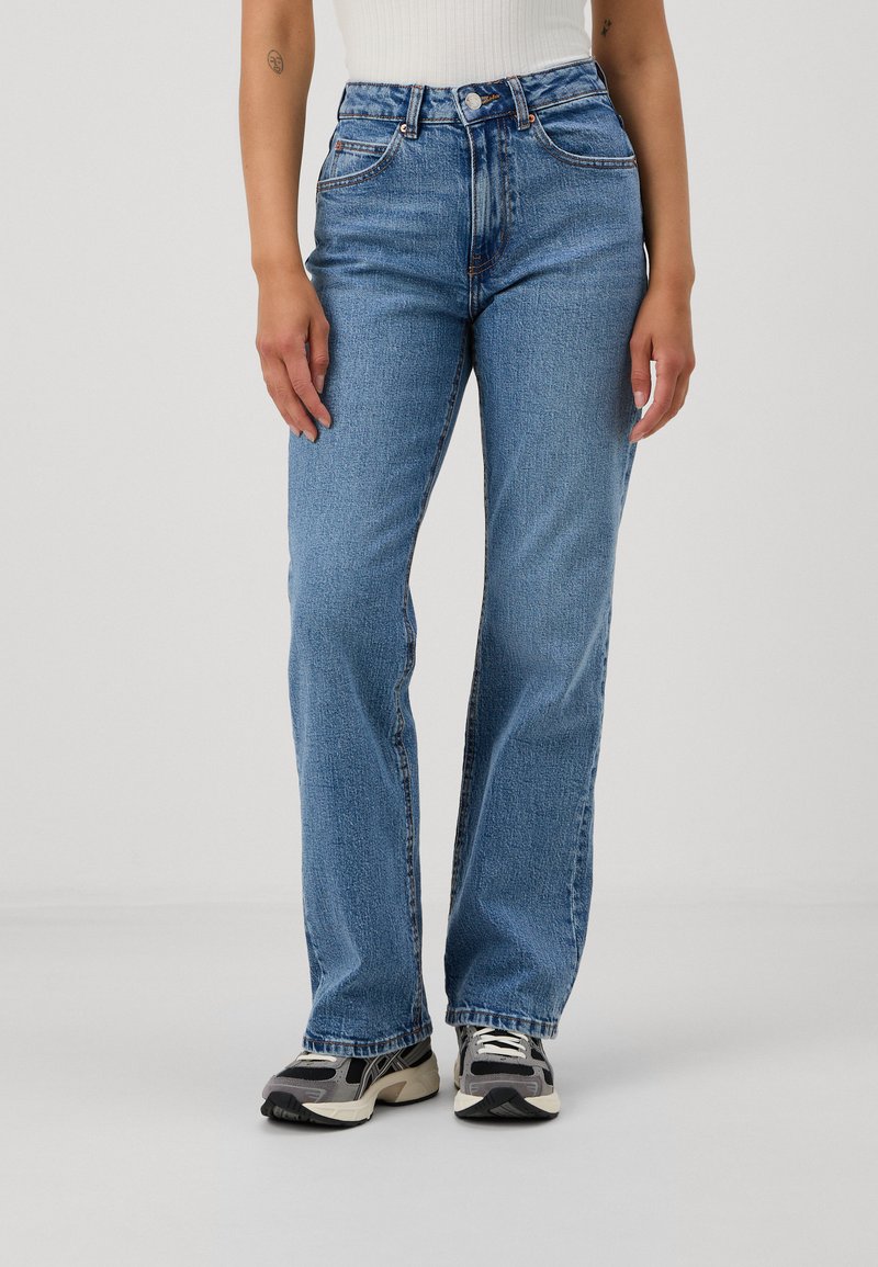 Jeans de denim azul de cintura alta com um corte reto, textura desbotada, costura visível e design clássico de cinco bolsos.