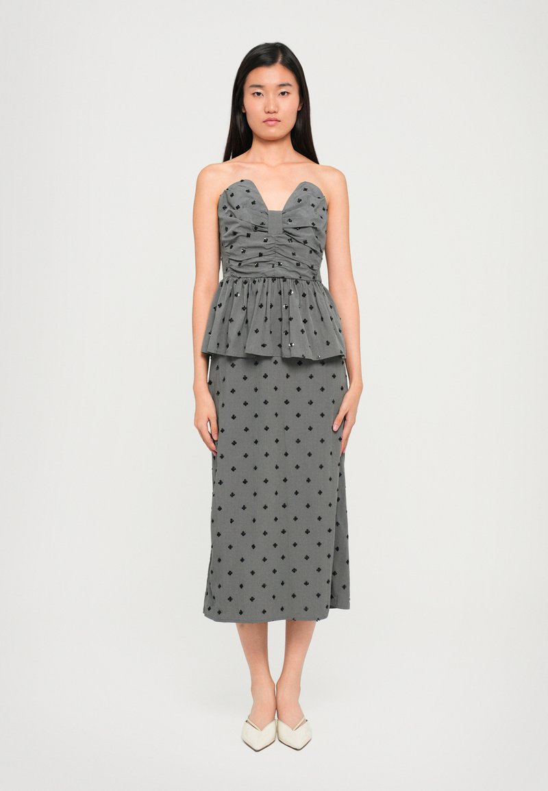 Γκρι φόρεμα peplum με λαιμόκοψη sweetheart, ραμμένο κορσέ και μαύρα διαμάντια, συνδυασμένο με λευκά παπούτσια με μυτερή μύτη.