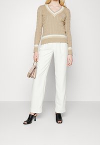 Beige kabelstickad tröja med V-ringning, vita ränder, kombinerad med vita vida byxor och svarta öppna klackar med gröna detaljer.