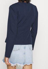 Haut à manches longues bleu marine avec un design ajusté. Texture lisse et silhouette cintrée, accompagné d'une jupe mini en denim clair avec des bords effilochés.