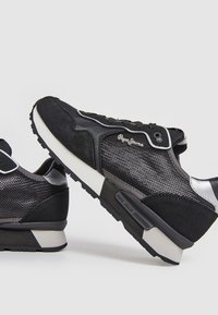 Black sneakers featuring a mix of mesh and suede materials, with a sleek design, reflective accents, and a textured rubber sole.
