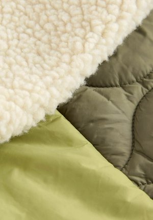 Fleece beige doux avec une surface texturée superposée à des tissus matelassés lisses en vert olive et en vert clair.