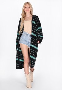 Mustat neuletakki, jossa on turkooseja ja valkoisia vaakaraitoja, pitkät hihat, auki oleva etuosa, yhdistetty beigeen toppiin ja kulutettuihin farkkushortseihin.