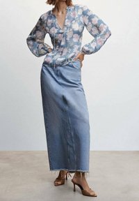 Blomstret bluse i blå og pink med lange ærmer, parret med en lang denimnederdel. Nederdelen har en rå søm og en afslappet pasform. Brune hælede sandaler.
