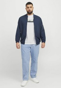 Námořnická bomber bunda s žebrovanými manžetami přes bílý tričko, spárována s světle modrými džíny a bílými teniskami. Minimalistický design, volný střih.