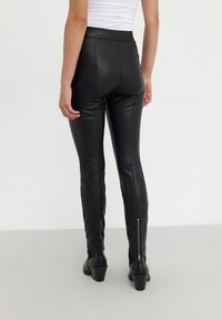 Pantalons skinny en simili cuir noir avec une taille haute, dotés de détails zippés sur les côtés aux chevilles et d'une texture lisse.