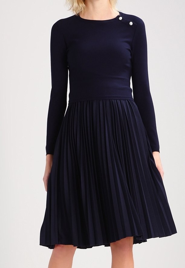 Robe bleu marine avec un haut ajusté à manches longues et une jupe plissée. Comprend deux boutons décoratifs près de l'épaule. Texture du tissu lisse.