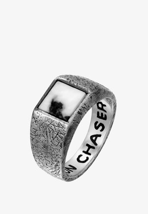 Bague carrée en métal argenté avec une surface texturée et un incrustation de pierres noir et blanc ; gravée avec le mot "CHASER" à l'intérieur de l'anneau.