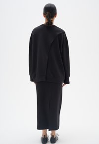 Sudadera negra de gran tamaño con una costura asimétrica única, combinada con una falda larga a juego. El material parece suave con una textura mínima.