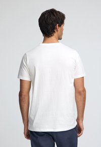 Biała bawełniana koszulka z krótkimi rękawami i okrągłym dekoltem, pokazana od tyłu, bez wzoru. Miękka tekstura i luźny krój.