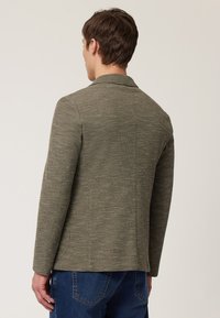 Groene textuur blazer met een getailleerde snit, met afgebroken kraag en twee zijzakken, gecombineerd met blauwe jeans.