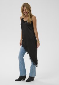 Schwarzes asymmetrisches Satin-Oberteil mit Spitzenbesatz, kombiniert mit hellblauen Schlagjeans und schwarzen Stiefeln mit Absatz. Einfaches, elegantes Design.