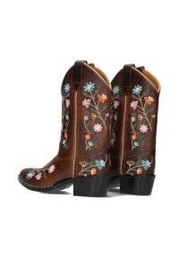Brown leather cowboy boots featuring colorful floral embroidery in pink, blue, and orange, with a low stacked heel and stitching detail.