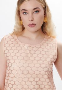 Top senza maniche color pesca con un motivo a rete geometrico, caratterizzato da una texture liscia e una leggera lucentezza. Collo rotondo e orlo morbido.