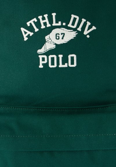Πράσινο ύφασμα με λευκό κεντημένο κείμενο "ATHL. DIV. POLO" και ένα φτερωτό αθλητικό παπούτσι με τον αριθμό 67 στο κέντρο.
