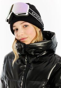 Zwarte donzen jas van glanzend materiaal met hoge kraag, gedragen onder een zwarte gebreide beanie. Skibril is op de beanie geplaatst.