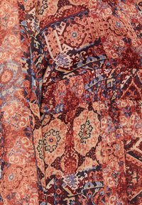 Tissu à motifs multiples avec des teintes rouges, oranges et bleues. Présente des designs complexes avec des formes florales et géométriques, et une taille élastique.