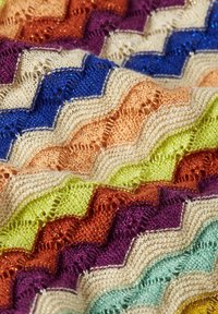 Gebreide stof met een zigzagpatroon in levendige kleuren: blauw, paars, oranje, groen en beige, met een gestructureerd, glanzend oppervlak.