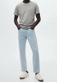 Camiseta gris de manga corta combinada con jeans rectos de mezclilla azul claro y zapatillas blancas con suelas marrones, en un fondo neutral.