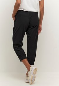 Schwarze, kurze Hosen mit elastischem Bund und umgeschlagenen Bündchen aus leichtem Stoff. Kombiniert mit weißen Sneakern.