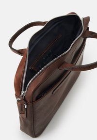 Bolso mensajero de cuero marrón con una parte superior con cremallera, dos asas y un bolsillo interior. Presenta una textura suave y detalles de cremallera plateados.