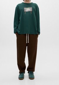 Grøn langærmet T-shirt med et retro fjernsynsdesign, parret med løse brune sweatpants og teal ruskindsko. Enkel design og komfortabel pasform.