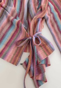 Knit fabric with horizontal stripes in pink, blue, purple, and tan tied in a bow, showing texture and ruffled edges.
