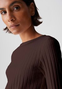 Dark brown ribbed long-sleeve top with a high neck, featuring a textured fabric that emphasizes vertical lines and a close-fitting silhouette.
