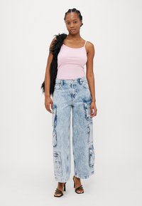 Lys rosa tettsittende tanktop kombinert med lyseblå oversized cargo-bukser som har flere lommer, en slitt vask og frynsete hem.