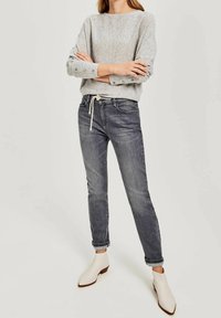 Szary sweter z dzianiny z podwiniętymi rękawami, w zestawieniu z ciemnoszarymi obcisłymi jeansami i białymi botkami na niskim obcasie.